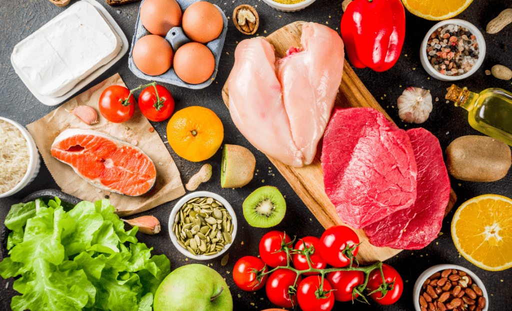 Zdrowe produkty leżące na stole w tym kurczak, pomidory, oliwa, łosoś kwiwi, papryka