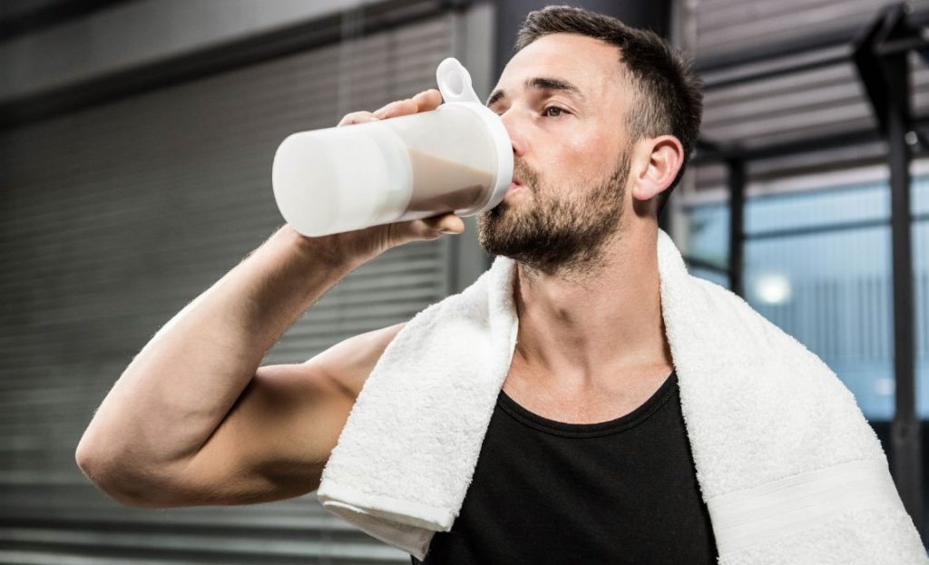 Mężczyzna po treningu na siłowni pije shake'a proteinowego. 